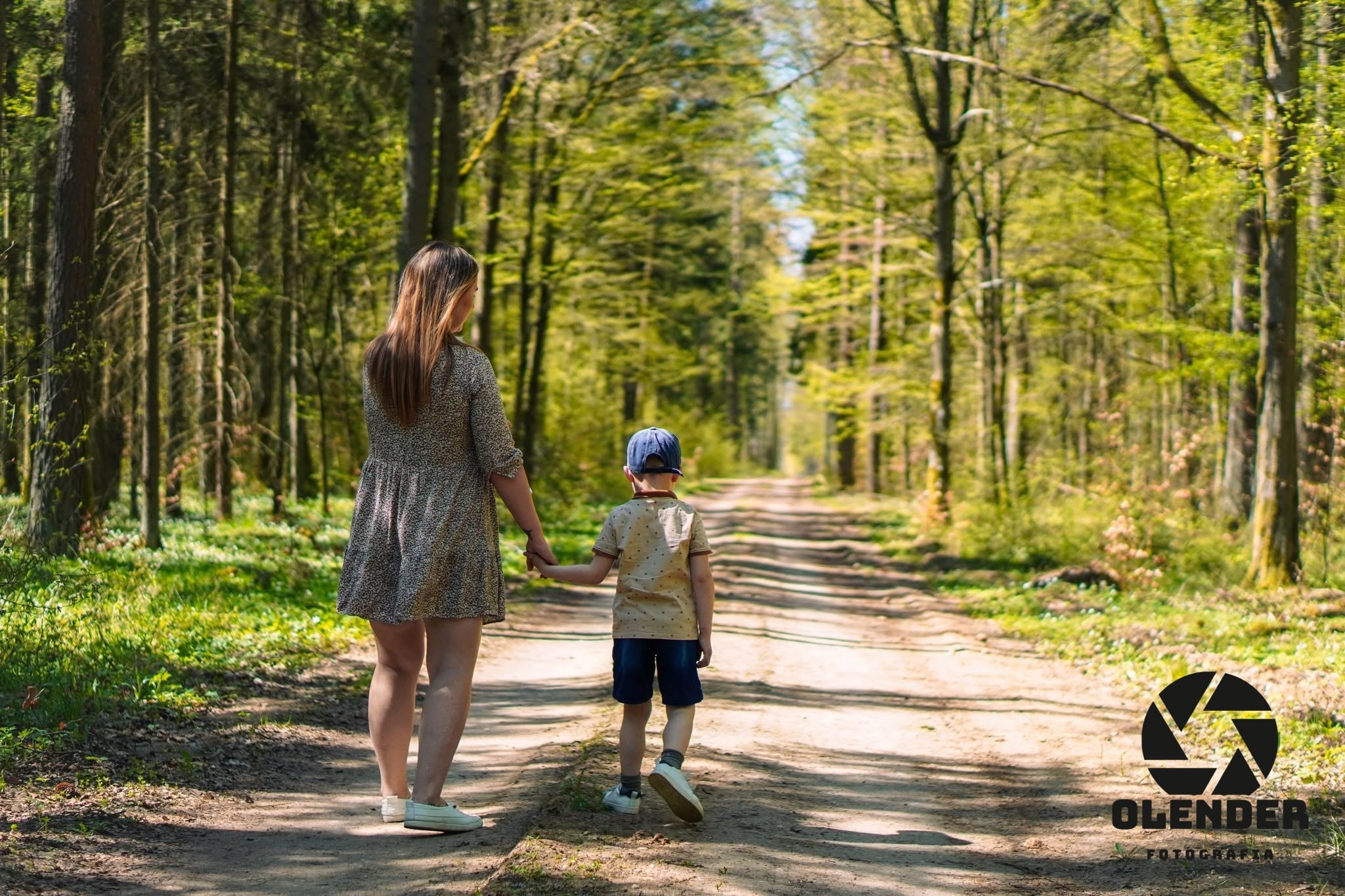 Mama prowadzi syna za rękę leśną drogą
